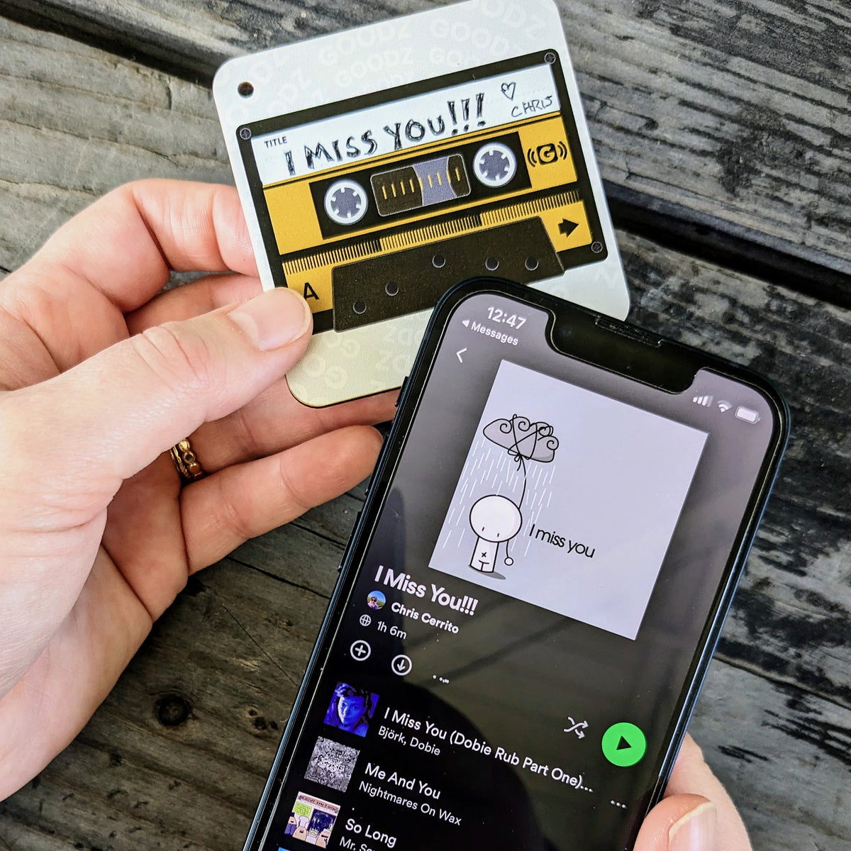 Hands holding a Mixtape Goodz labeled I Miss You next to a phone playing the playlist